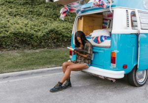 A woman reading while sat on the bumper of her campervan