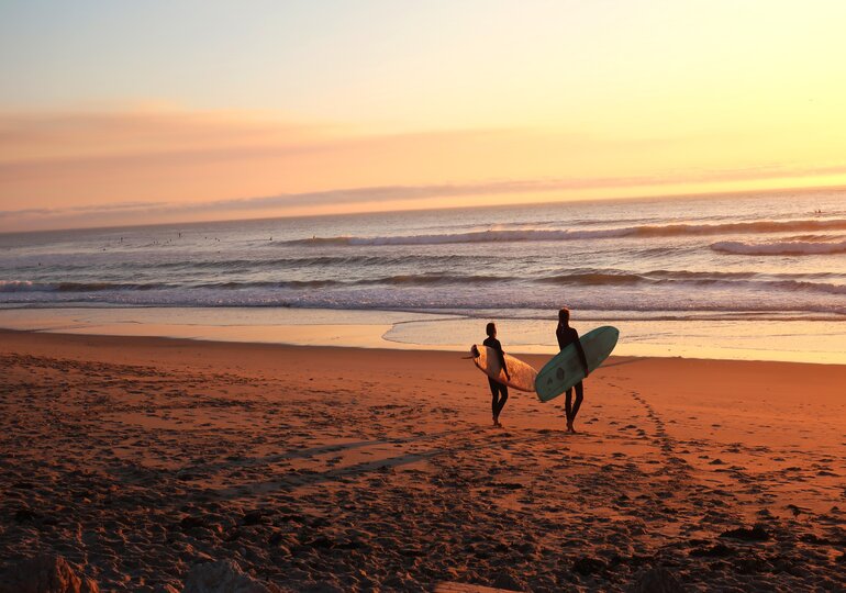 surfers on a beach at sunset