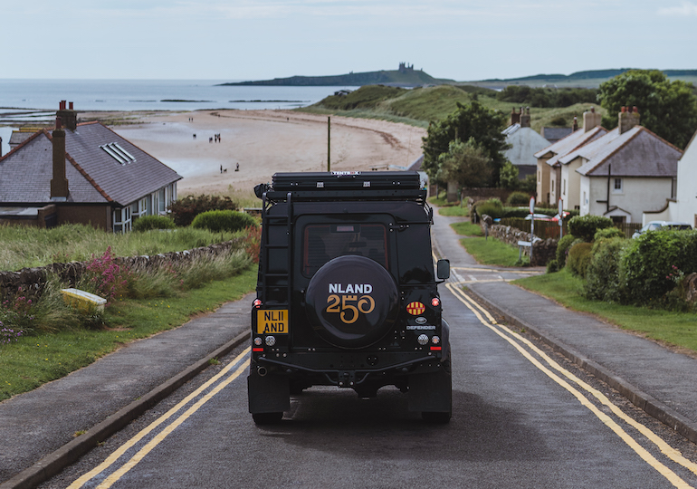 Defender driving down hill with beach behind
