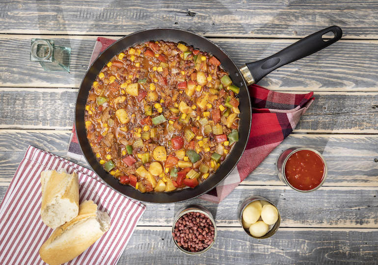 A pan of cowboy stew surrounded by canned ingredients