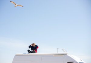 Woman sat atop a campervan looking at a bird through binoculars