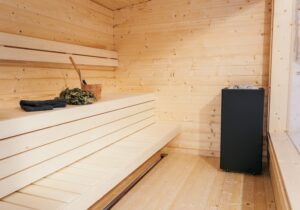 The wooden interior of a sauna, complete with stove, wooden bucket and sauna whisk