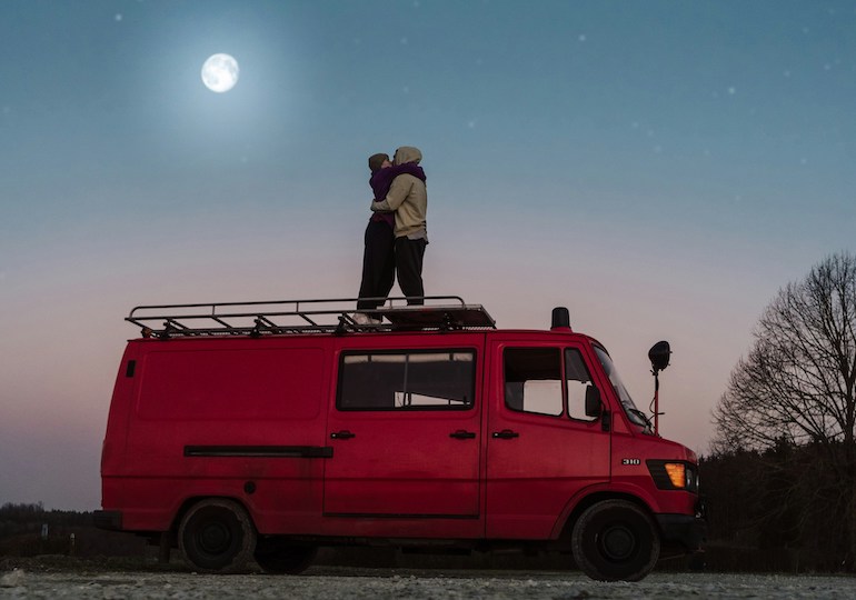 Couple standing on top of a Campervan kissing under a full moon
