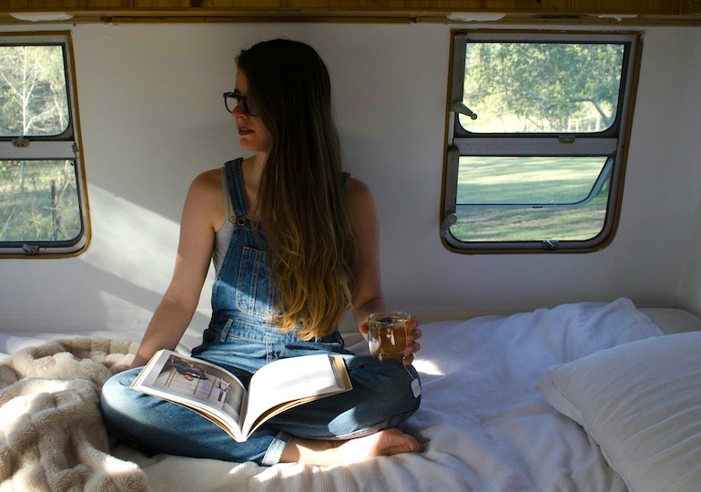 A woman with a cup of tea and an open book inside a caravan