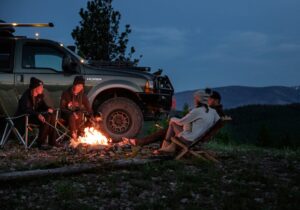 Three people sitting around a campfire with the front of their overland in view in the background