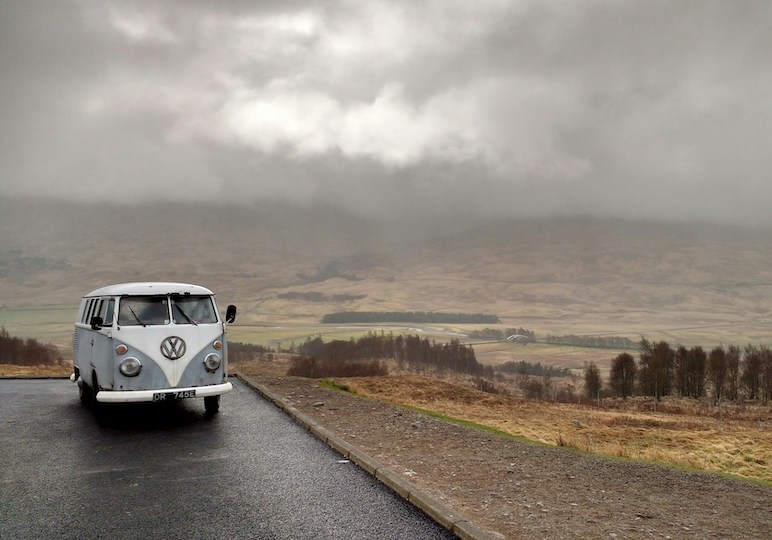 Old VW campervan driving along a road in Scotland