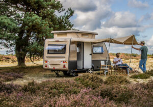 A Kip caravan parked up under a tree with a man relaxing beneath its awning.