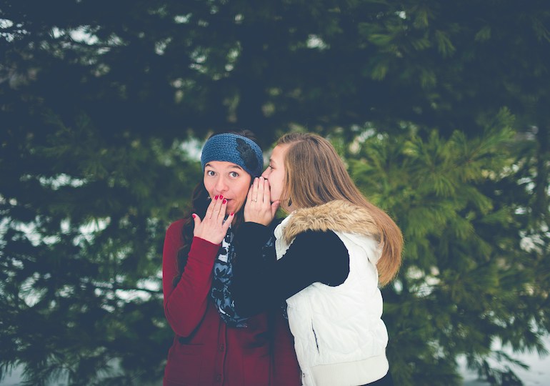 A woman whispering into another woman's ear